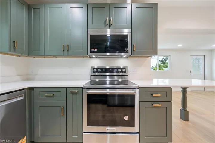 Kitchen featuring stainless steel appliances, green cabinetry, light stone counters, and recessed lighting