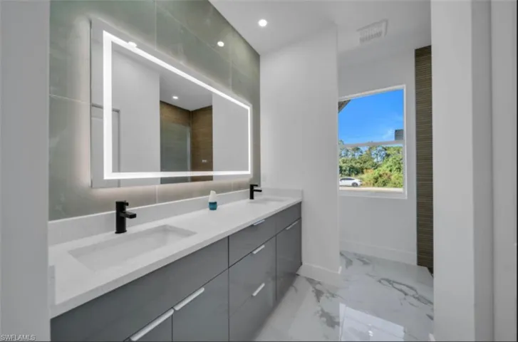 Bathroom with double vanity, light marble finish floors, and recessed lighting