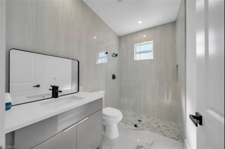 Bathroom featuring vanity, a walk in shower, light marble finish flooring, recessed lighting, and tile walls