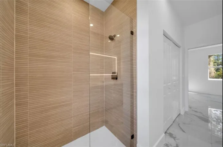 Full bath featuring tiled shower, light marble finish floors, and a closet