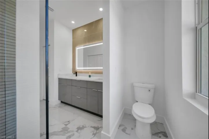 Bathroom with double vanity, light marble finish floors, and recessed lighting