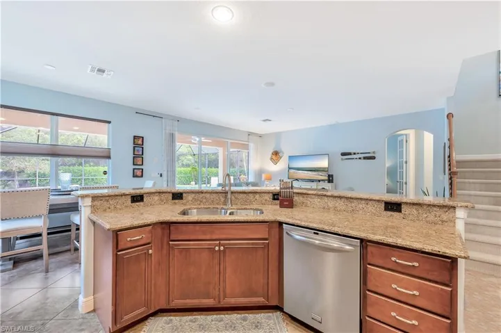 Kitchen with stainless steel dishwasher, light stone countertops, brown cabinetry, arched walkways, and light tile patterned flooring