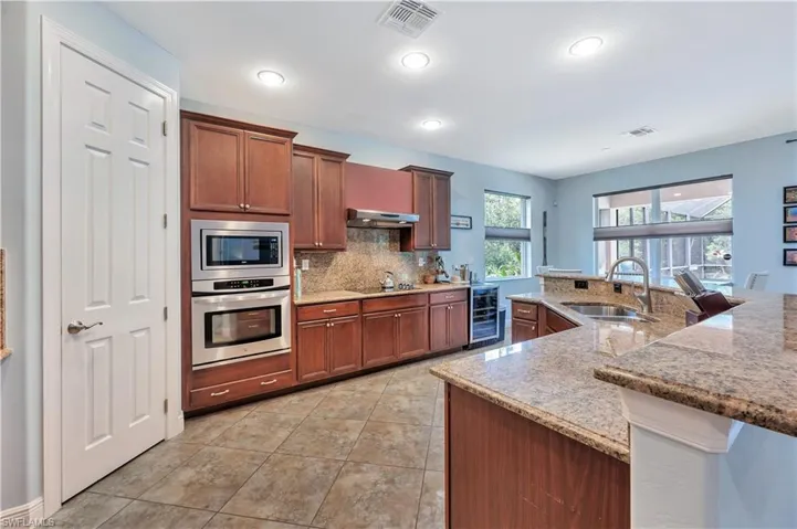 Kitchen featuring stainless steel appliances, beverage cooler, under cabinet range hood, tasteful backsplash, and light stone countertops