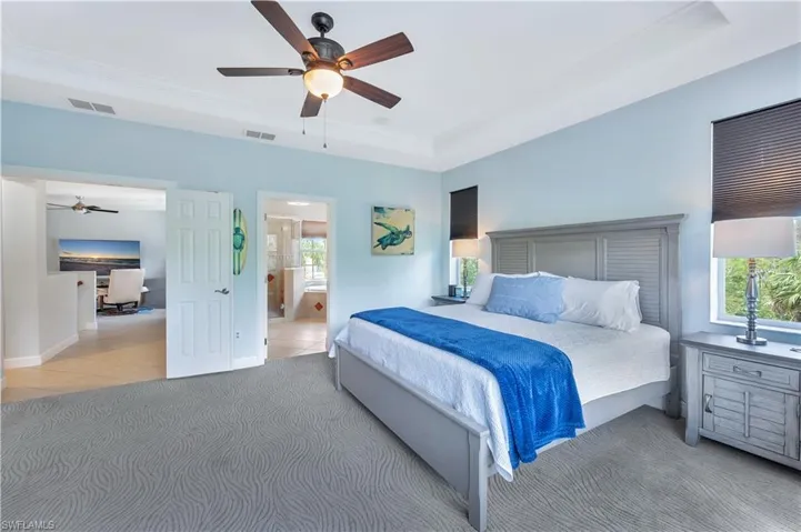 Tiled bedroom featuring a tray ceiling, crown molding, ceiling fan, ensuite bath, and an office area