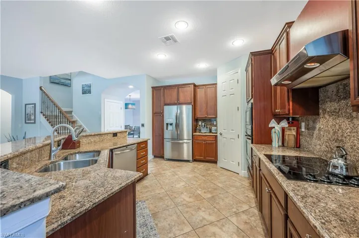 Kitchen featuring appliances with stainless steel finishes, wall chimney exhaust hood, arched walkways, decorative backsplash, and light stone counters