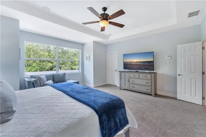 Bedroom with a raised ceiling, carpet flooring, and a ceiling fan
