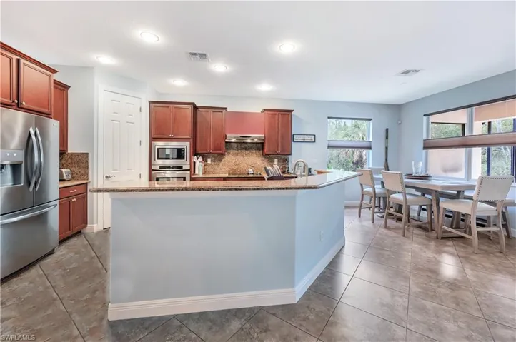 Kitchen featuring appliances with stainless steel finishes, tasteful backsplash, a center island with sink, recessed lighting, and brown cabinetry