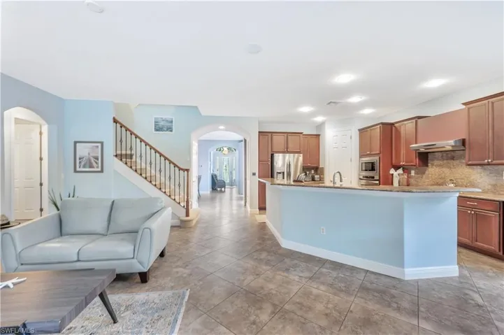 Kitchen with arched walkways, stainless steel appliances, an island with sink, decorative backsplash, and under cabinet range hood