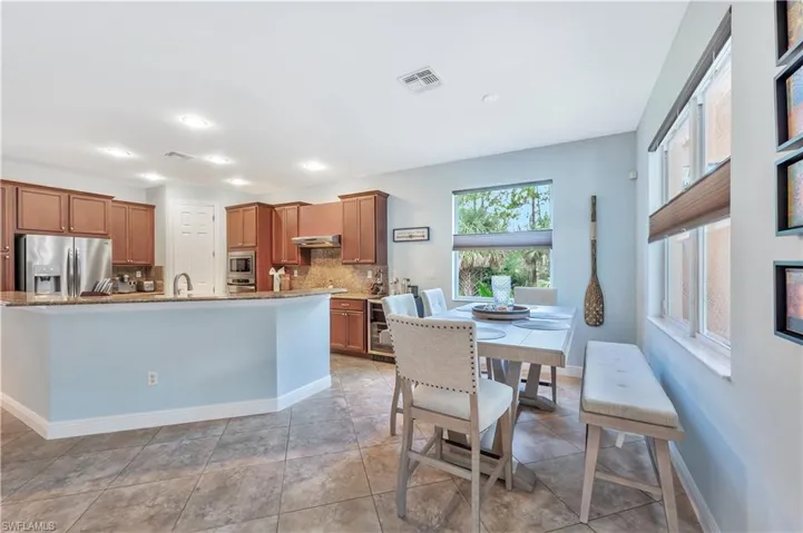 Kitchen featuring appliances with stainless steel finishes, decorative backsplash, brown cabinets, a kitchen island with sink, and recessed lighting