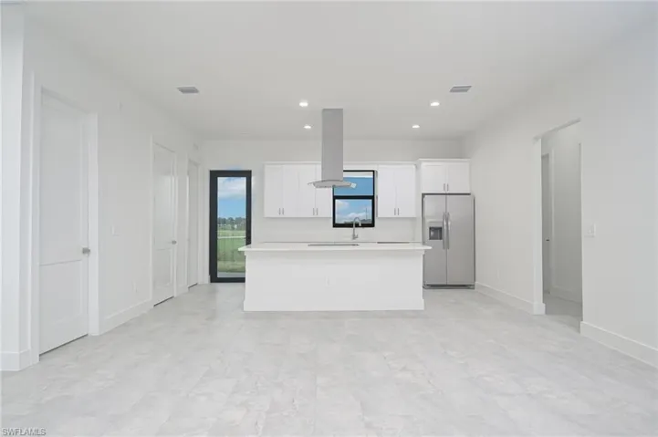 Kitchen with stainless steel refrigerator with ice dispenser, island range hood, white cabinetry, a center island, and light tile floors