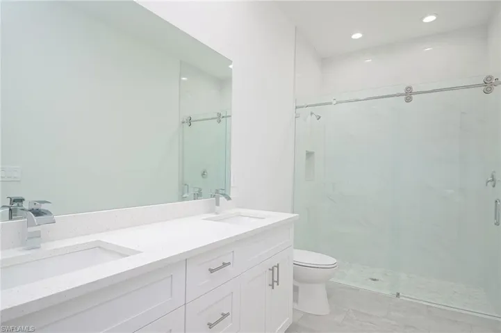 Bathroom featuring double vanity, an enclosed shower, tile flooring, and toilet