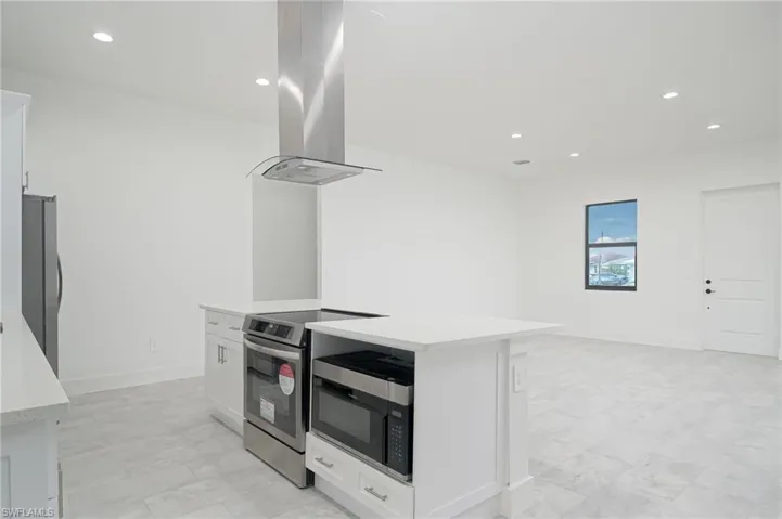 Kitchen featuring a center island, island range hood, stainless steel appliances, white cabinets, and light tile floors