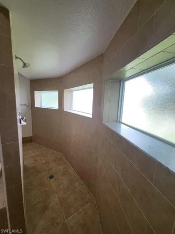 Bathroom featuring a tile shower, a textured ceiling, and tile walls