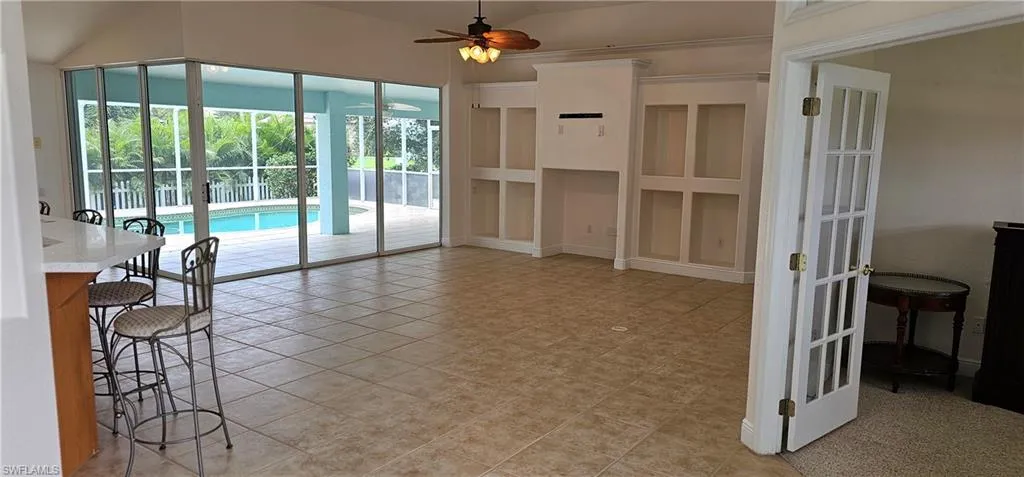 Empty room with light tile patterned flooring, lofted ceiling, ceiling fan, and french doors