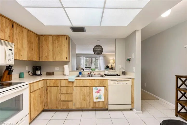 Kitchen with white appliances, light countertops, light tile patterned floors, and light wood finish cabinets