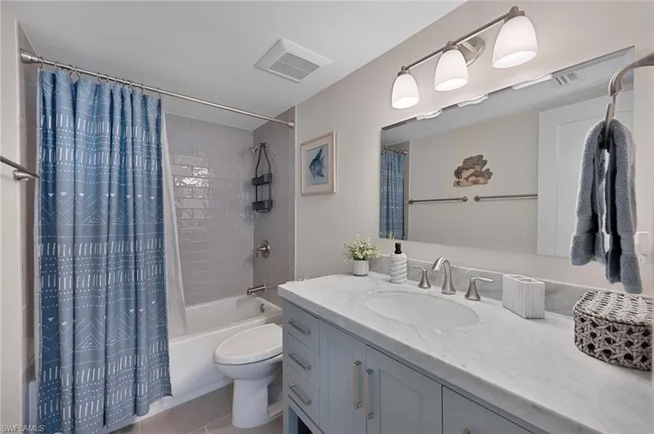 Full bath featuring tile patterned floors, visible vents, toilet, vanity, and shower / tub combo with curtain