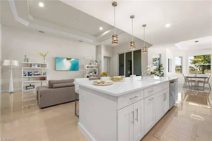 Kitchen with a tray ceiling, open floor plan, white cabinets, a center island with sink, and decorative light fixtures