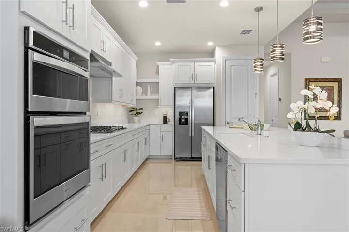 Kitchen with stainless steel appliances, white cabinets, a kitchen island with sink, open shelves, and hanging light fixtures