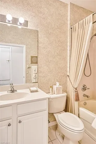 Full bath with light tile patterned floors, shower / bath combo, vanity, and wallpapered walls