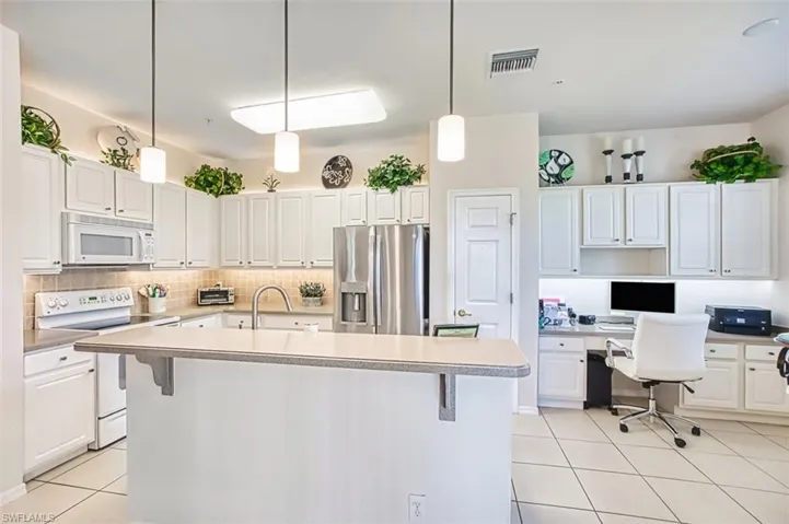 Kitchen with light tile patterned flooring, white appliances, built in study area, white cabinetry, and pendant lighting