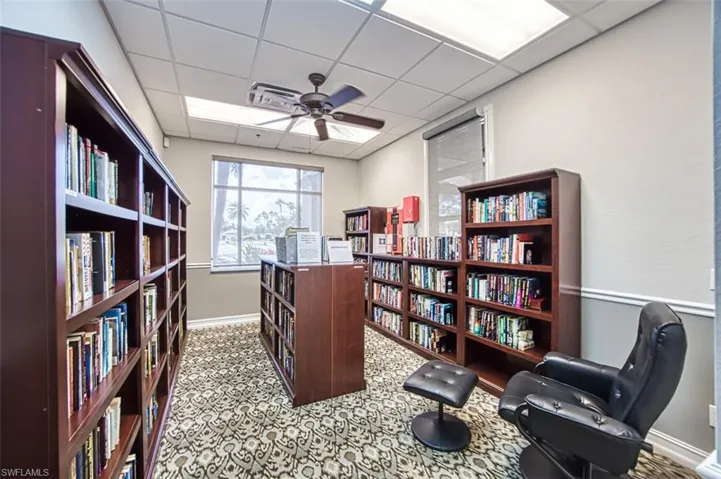 Sitting room featuring a drop ceiling, wall of books, and a ceiling fan