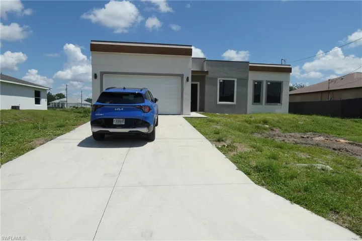 Modern facade featuring a flat roofline with a wood-finish accent, attached garage with a white door, concrete driveway, and multiple dark-framed windows