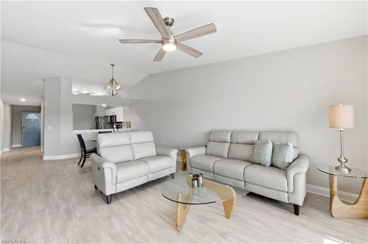Living room featuring light wood-style flooring, ceiling fan, vaulted ceiling, and a chandelier