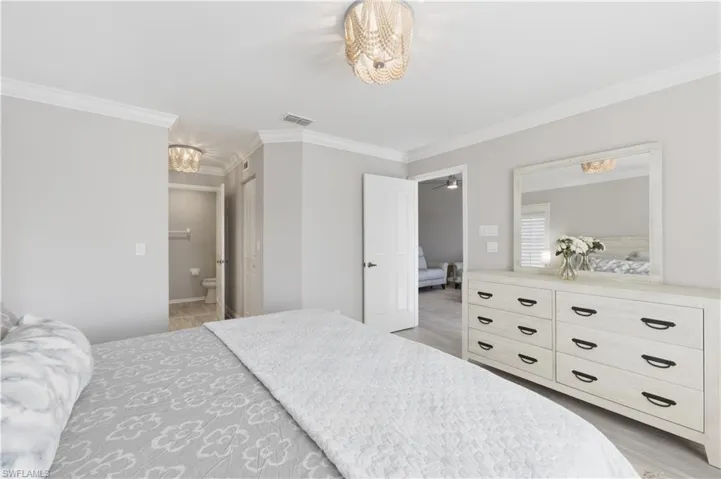 Bedroom featuring suspended lighting, ornamental molding, ensuite bath, a closet, and light wood-style flooring