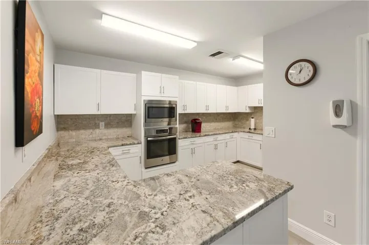 Kitchen with white cabinets, light stone countertops, stainless steel appliances, backsplash, and a peninsula
