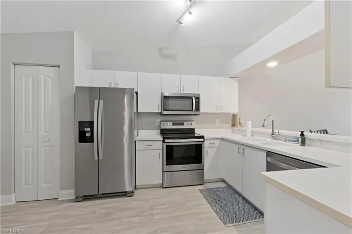 Kitchen with stainless steel appliances, light countertops, light wood-type flooring, white cabinets, and rail lighting