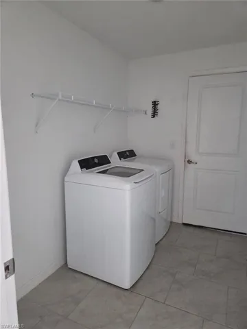Laundry area with washing machine and clothes dryer and light tile patterned flooring