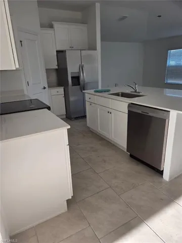 Kitchen with white cabinets, appliances with stainless steel finishes, a center island with sink, and light tile patterned floors