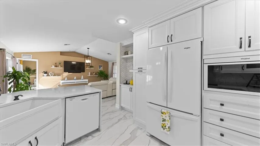 Kitchen featuring white appliances, white cabinetry, vaulted ceiling, open shelves, and light stone countertops