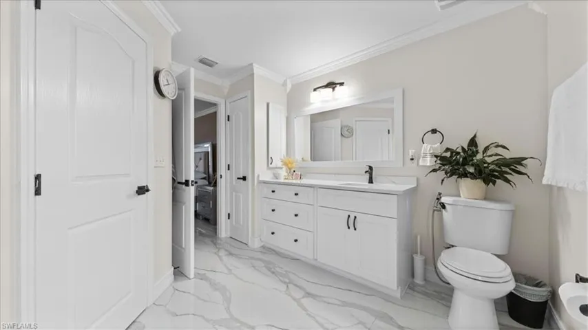Full bath with vanity, crown molding, and light marble finish flooring