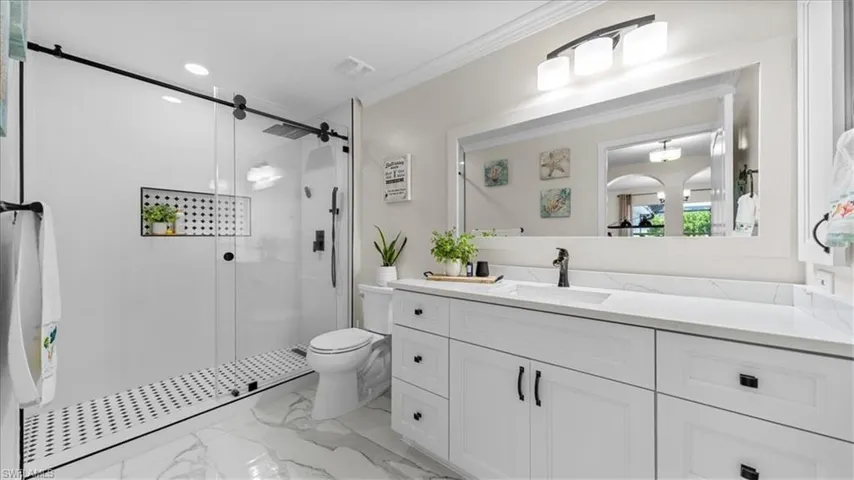 Full bathroom featuring a stall shower, vanity, light marble finish floors, ornamental molding, and recessed lighting