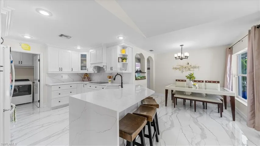 Kitchen with backsplash, a breakfast bar, freestanding refrigerator, light stone countertops, and a chandelier