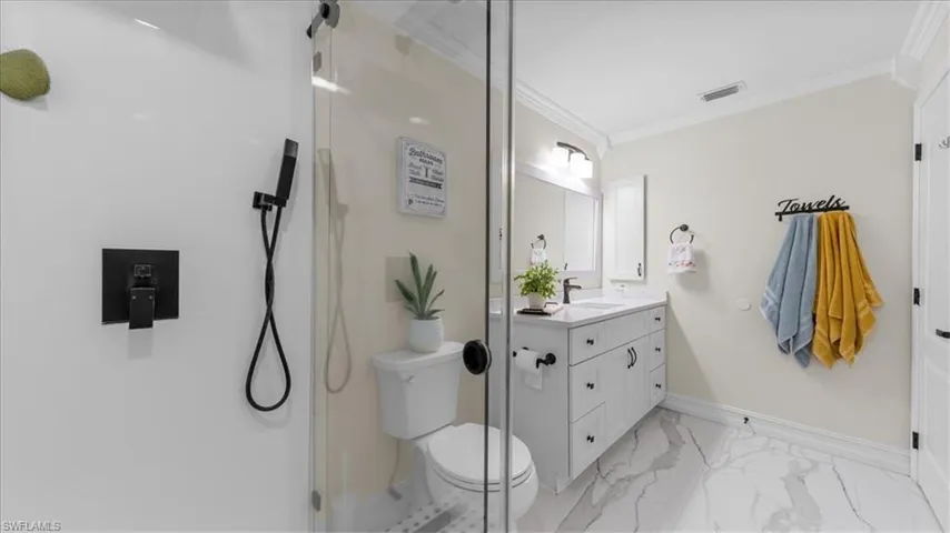 Bathroom featuring crown molding, vanity, a shower with door, and light marble finish flooring