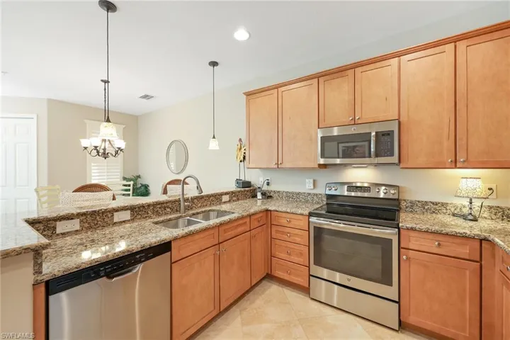 Kitchen with pendant lighting, sink, light stone countertops, appliances with stainless steel finishes, and a chandelier