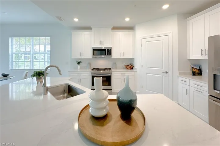 Kitchen with stainless steel appliances, white cabinetry, light stone countertops, and recessed lighting
