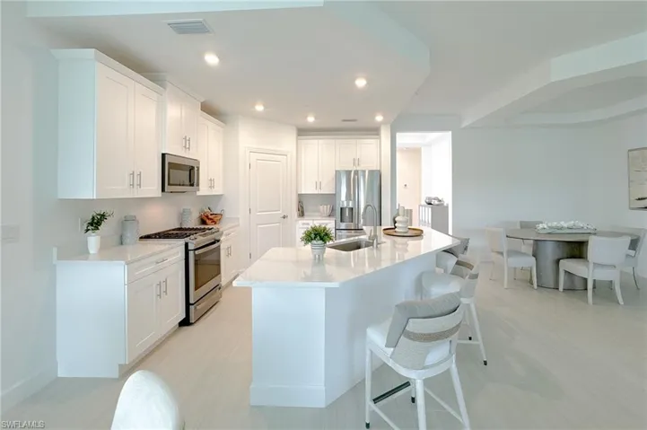 Kitchen with stainless steel appliances, white cabinets, light stone countertops, an island with sink, and a breakfast bar