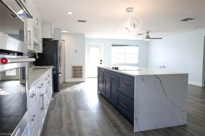 Kitchen featuring two tone color scheme, stainless steel appliances, dark wood finished floors, light stone countertops, and ceiling fan