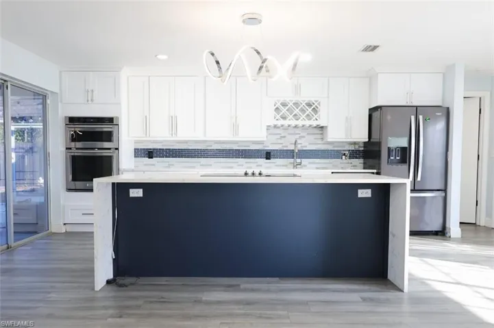 Kitchen with white cabinetry, stainless steel appliances, light stone counters, and pendant lighting