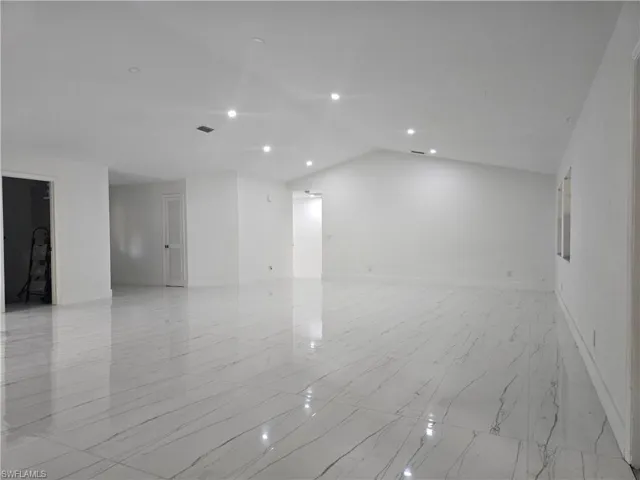 Empty room with recessed lighting, marble finish floor, baseboards, and lofted ceiling