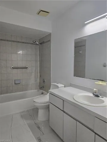 Bathroom featuring visible vents, toilet, vanity, marble finish floor, and bathing tub / shower combination