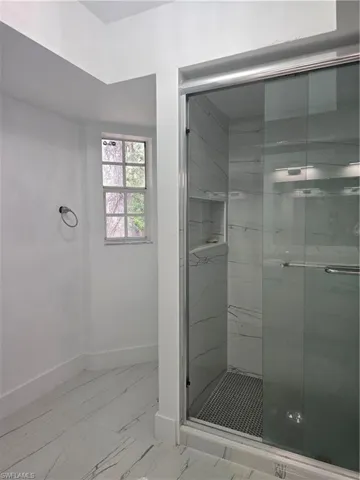 Bathroom featuring a shower stall, marble finish floor, and baseboards