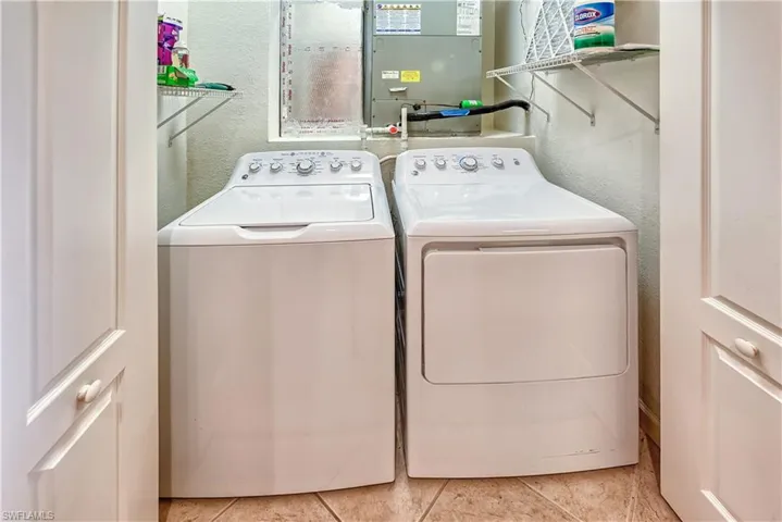 Washroom featuring a textured wall, heating unit, washing machine and dryer, and light tile patterned floors