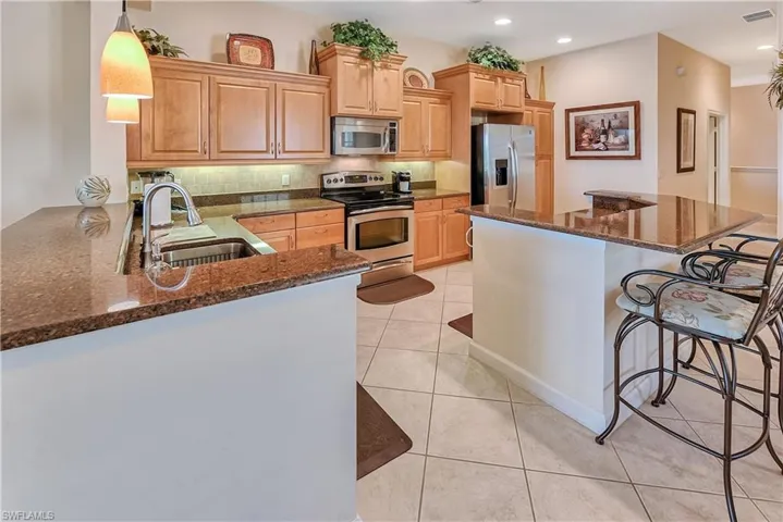 Kitchen featuring decorative light fixtures, a kitchen bar, tasteful backsplash, dark stone counters, and stainless steel appliances