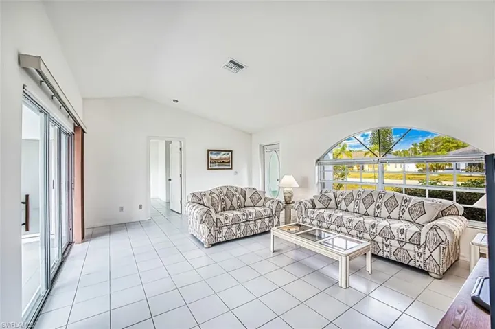 Living room featuring light tile patterned floors, vaulted ceiling, and visible vents