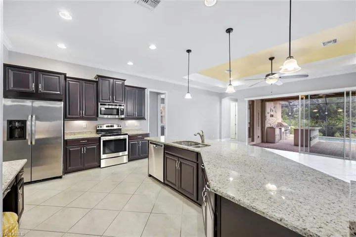 Gourmet kitchen with stainless steel appliances, a raised ceiling, hanging light fixtures and granite countertops