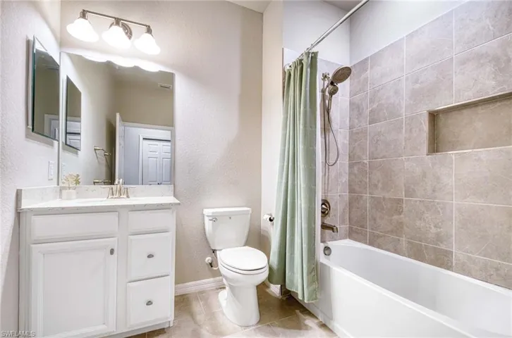 Full bathroom featuring shower / bath combo, a textured wall, vanity, and light tile patterned flooring